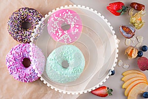 Colorful doughnuts with different kinds of topping and fruits on light background with place for text.