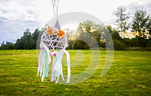 Colorful dreamcatcher on summer nature background. Handmade decor made of feathers, ribbons, threads and beads