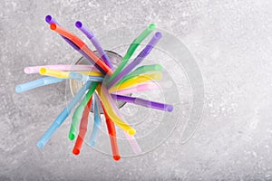 Colorful drinking straw in glass on grey background, top view.