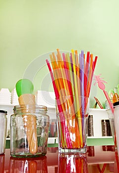 Colorful drinking straws in glass, plastic spoon and plastic spatula tool kitchenware for ice cream.