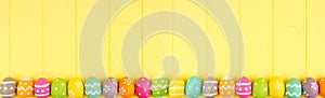 Colorful Easter banner with a row border of Easter Eggs over a yellow wood background with copy space