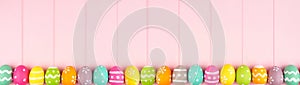 Colorful Easter banner with a row border of Easter Eggs over a pink wood background with copy space