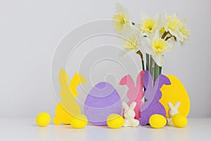 Colorful Easter bunnies, eggs and bouquet of daffodils on white background with space for text. Happy Easter! Pink and yellow