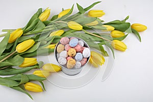 Colorful Easter candy eggs with yellow tulips isolated on white