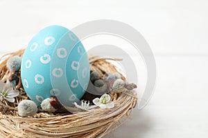Colorful Easter egg in decorative nest on wooden table, closeup. Space for text
