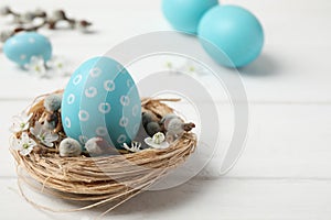 Colorful Easter egg in decorative nest on wooden table. Space for text