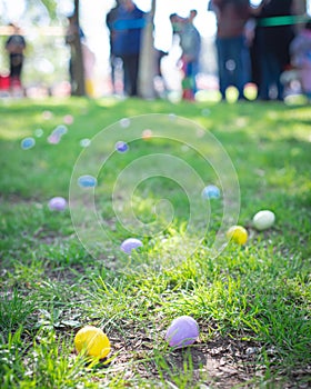 Colorful Easter egg on green grass meadow with blurry long line of diverse kids parents waiting for egg hunt tradition