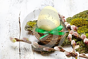 Colorful easter egg in nest and branch on white wooden table