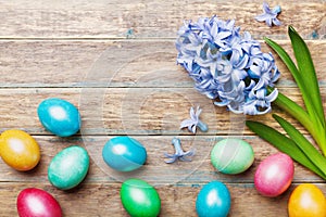 Colorful Easter eggs background with flowers on wooden rustic table top view. Spring greeting card for holiday.