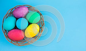 Colorful easter eggs in a basket on a blue color background with a copyspace