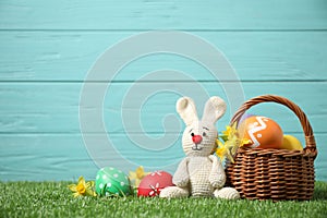 Colorful Easter eggs, basket and bunny toy on grass against light blue wooden background