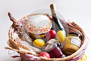 Colorful easter eggs in a basket with cake, red wine, hamon or jerky and dry smoked sausage on white background.