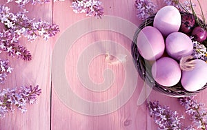 Colorful easter eggs in basket on wooden table.Holiday background with spring lilac flowers. Top view with copy space