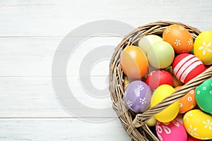 Colorful Easter eggs in basket on white wooden table, top view. Space for text