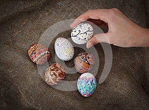 Colorful Easter eggs on burlap, female hand chose and pick one