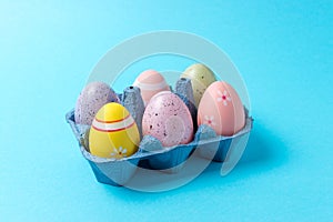 Colorful Easter eggs in carton tray on blue background. Minimal concept