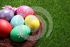 Colorful Easter eggs in decorative nest on grass, closeup. Space for text