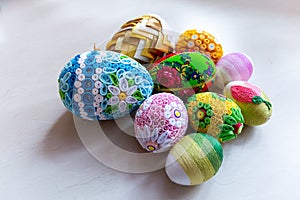 Colorful Easter eggs with floral ornaments, origami decorations and crewel wool against white background