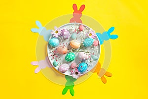 Colorful easter eggs with flowers on ceramic plate with paper bunnies on yellow background