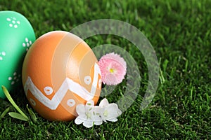 Colorful Easter eggs and flowers on grass, closeup. Space for text