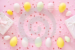 Colorful Easter eggs frame with bunny ears sugar sprinkle and gift box on pink background.