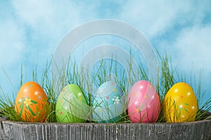 Colorful Easter eggs in grass on blue sky background. Copy space