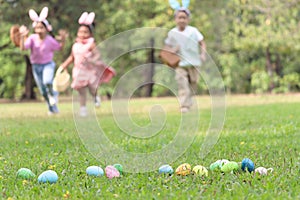 Colorful Easter eggs on green grass backyard with blurred background children with bunny ears holding basket, running to pick up