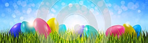 Colorful Easter Eggs On Green Grass Over Blue Bokeh Background Horizontal Banner