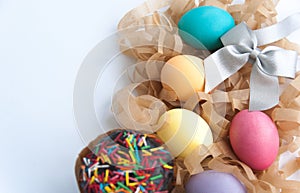 Colorful easter eggs on hay, easter cake and silver bow on white background. Copy space