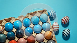 Colorful Easter eggs lie in a row on a blue background, top view with copy-space