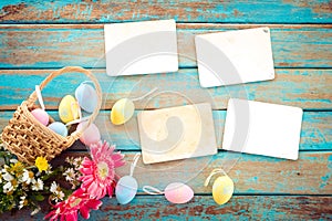 Colorful Easter eggs in nest with flower and empty old paper photo album on wood table