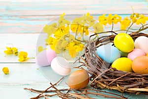 Colorful Easter eggs in nest with flower on rustic wooden planks background.