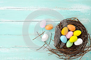 Colorful Easter eggs in nest with flower on rustic wooden planks background in blue paint.
