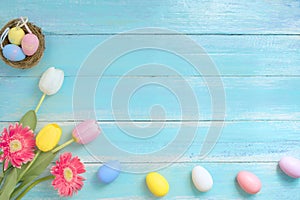 Colorful Easter eggs in nest with flowers on blue wooden background.