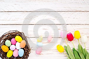 Colorful Easter eggs in nest with tulip flower on rustic wooden planks background.