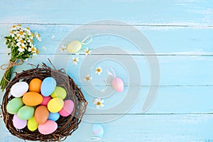 Colorful Easter eggs in nest with wildflowers on on rustic wooden planks background in blue paint.