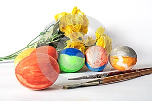 Colorful easter eggs with paint brushes and yellow flowers on a white background