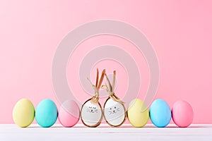 Colorful easter eggs with painted faces and bunny ears in row on a pink background