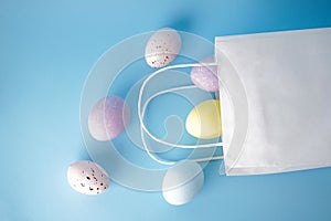 Colorful easter eggs and paper bag on blue background, flat lay