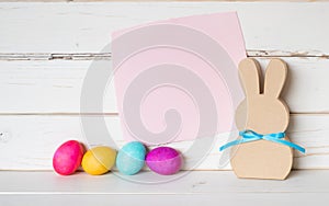 Colorful Easter Eggs with Pink Paper Invite Card and a Simple Bunny against White Shiplap Board Background wall