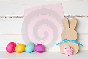 Colorful Easter Eggs with Pink Paper Invite Card and a Simple Bunny and Chick against White Shiplap Board Background wall
