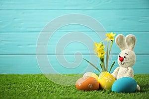 Colorful Easter eggs, rabbit and narcissus flowers in green grass against light blue background