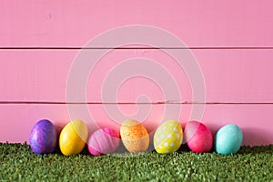 Colorful Easter Eggs in Row on Bottom of Pink Wood Boards Wall Background and Laying in Green Grass with room or space for copy