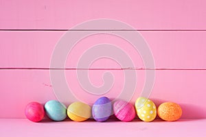 Colorful Easter Eggs in a Row on a Table and against a Bright Pink Board Wall Background with copy space. Horizontal and wide with