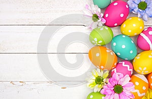 Colorful Easter eggs and spring flowers side border against a white wood background