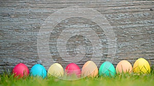 Colorful easter eggs stand in a row on a meadow on a wooden background.
