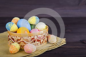 Colorful Easter eggs in wicker basket on textile on dark wooden