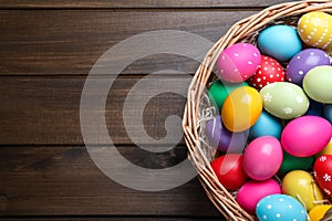 Colorful Easter eggs in wicker basket on wooden table, top view. Space for text