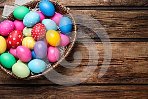 Colorful Easter eggs in wicker basket on wooden table, top view. Space for text