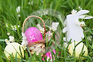 Colorful easter eggs, wooden rabbit and flowers on fresh spring grass in the garden.